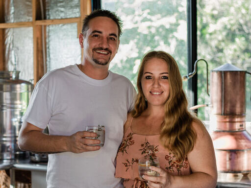 A portrait of Neddy and Christian Bedwell holding a drink each in their distillery