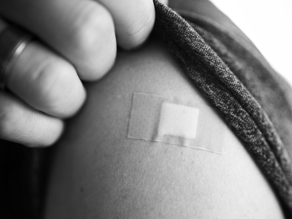 A close-up of a bandaid on a young person's upper arm, just below shoulder. 