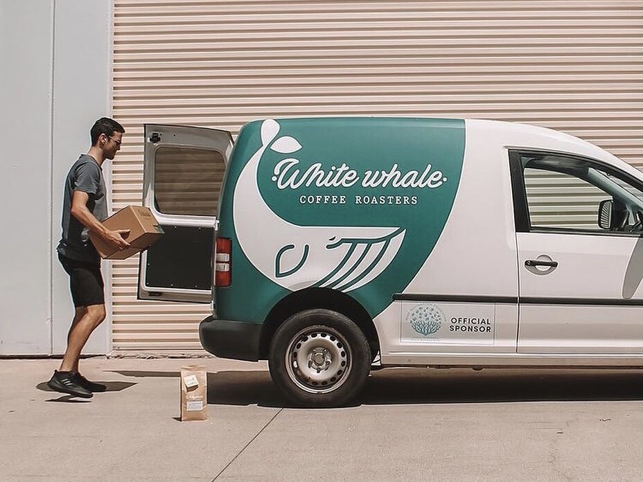 Someone loading boxes of coffee beans into the back of a van branded with White Whale Coffee Roasters