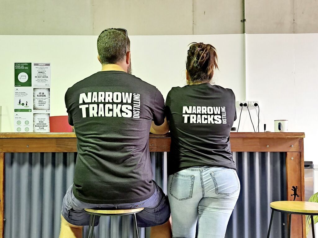 Narrow Tracks Distilling founders Doug Thorpe and Bec Zammit wearing t-shirts with branding on the back, not facing the camera.