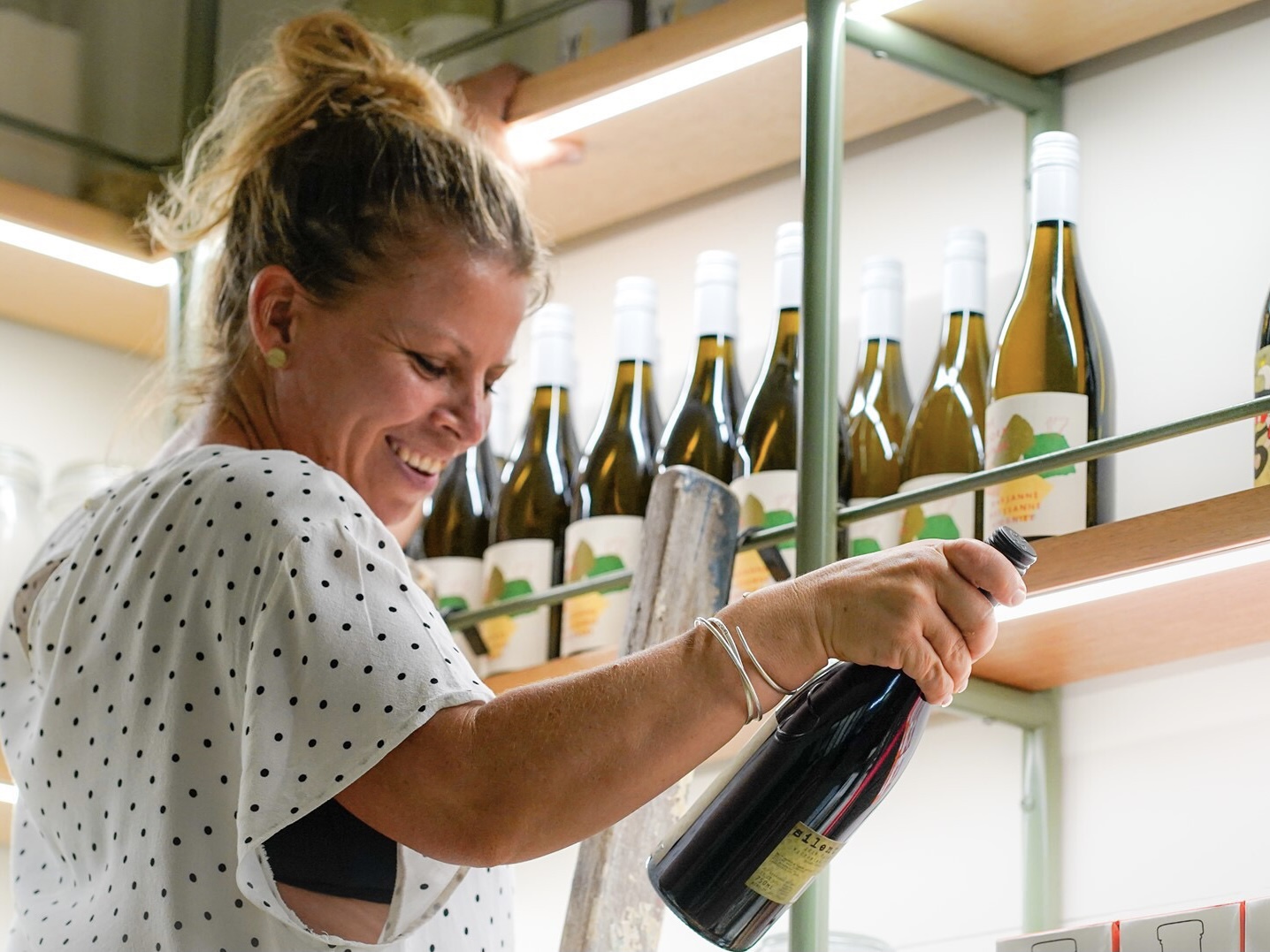 A woman pulling a bottle of wine down from a shelf