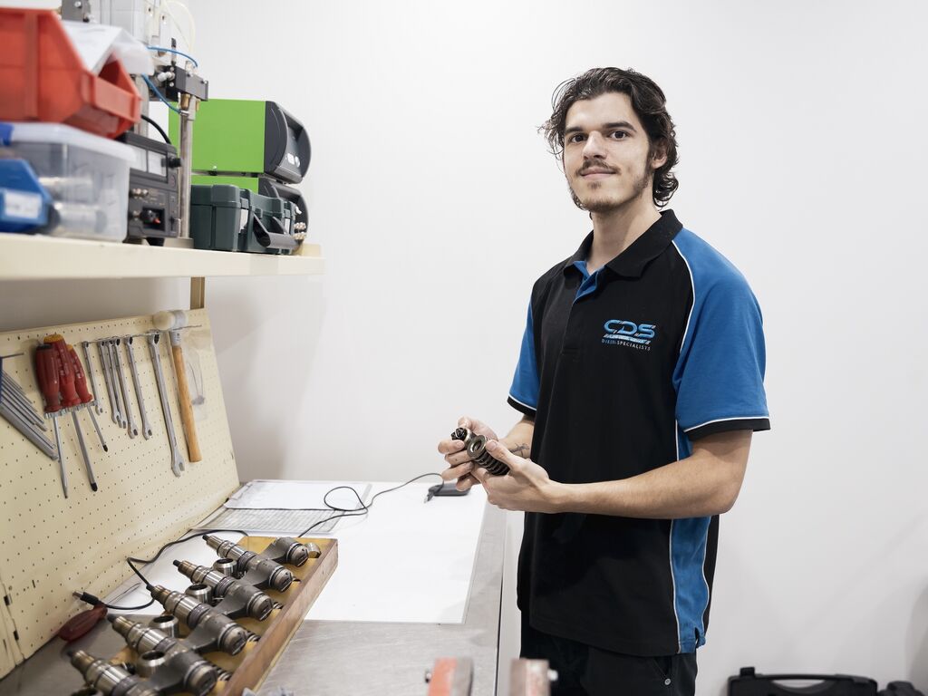 Darnell Creed-Wray, who has undertaken VPG's Learner Driver Program, has now secured an apprenticeship at Cairns Diesel Service. Image is of Darnell standing in the workshop smiling at the camera