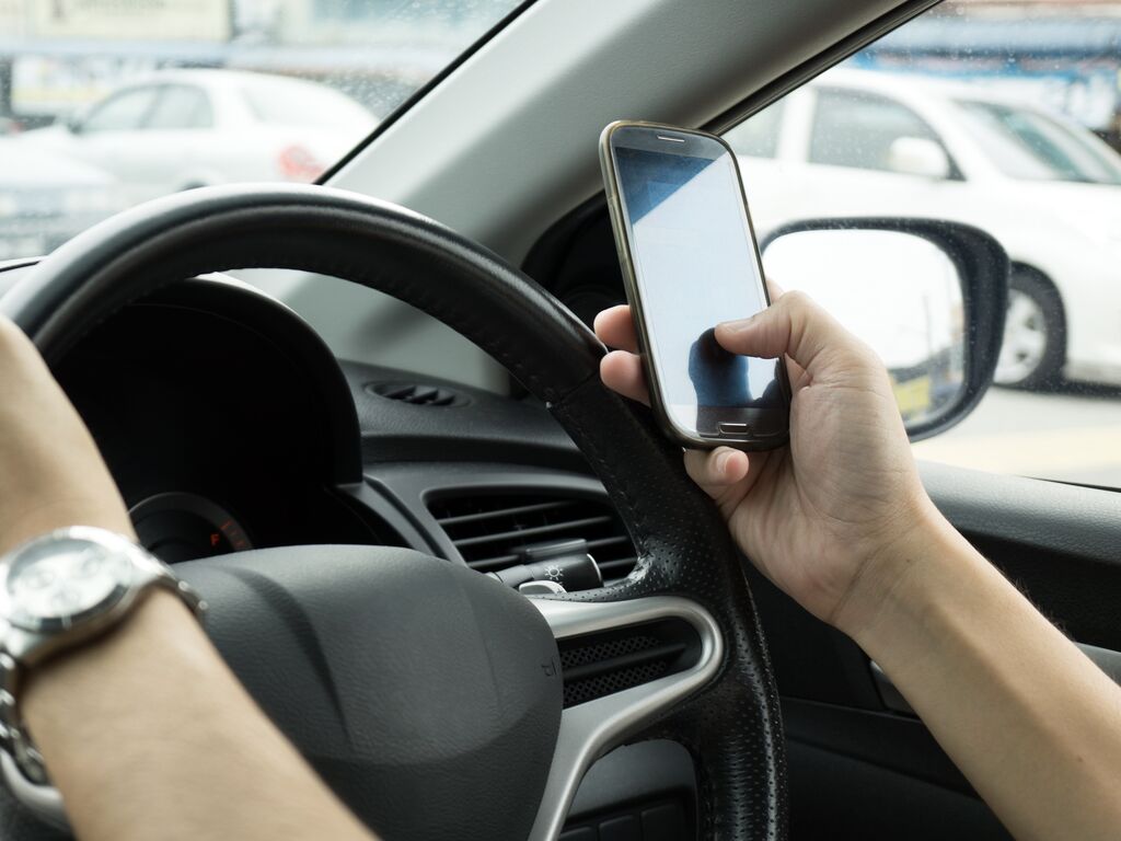 Close up of someone holding a phone in front of the wheel while driving