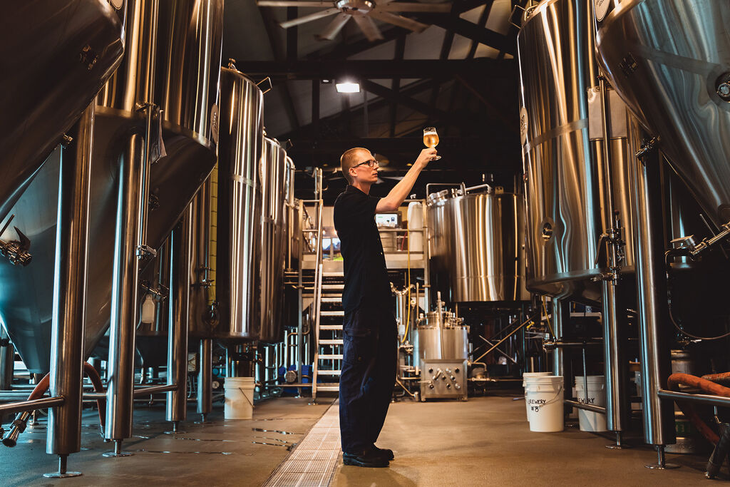 Head brewer Nico Leffler holding up a glass of beer to the light in the brewery 