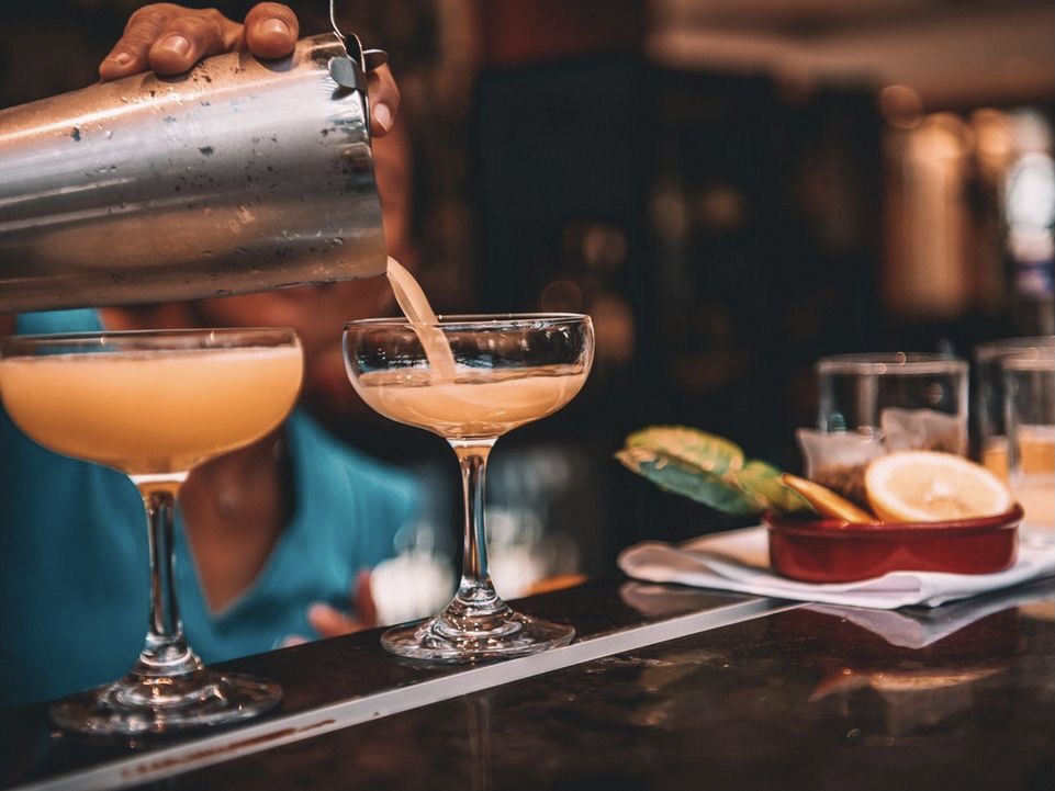 A close up of an orange cocktail being made in a dimly lit bar